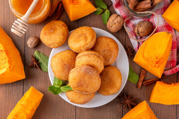 Autumn pumpkin pie donuts with cinnamon sugar sprinkled topping and pumpkin spice filling, on white wooden table with honey and pumpkin squash slices, copy space