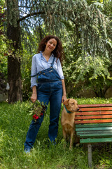 pretty smiling middle-aged woman with red hair in company with her dog sitting near a red and green bench