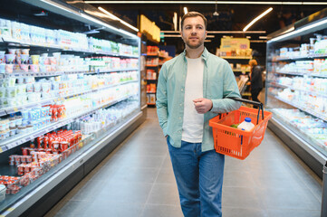 Customer walking through supermarket aisles holding shopping basket