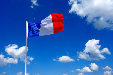 The flag of France flutters in the wind in a blue sky with white clouds