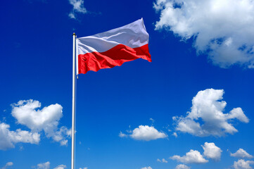 The flag of Poland flutters in the wind in a blue sky with white clouds
