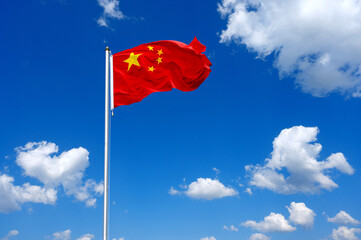 The flag of China  flutters in the wind in a blue sky with white clouds
