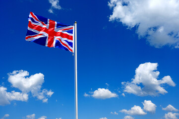 flag of United Kingdom fluttering in the blue sky with cumulus clouds