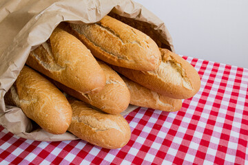 Fresh baguettes in paper bag on red and white checkered tablecloth