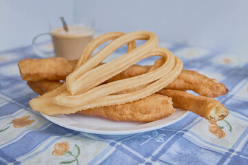 Typical Madrid breakfast, churros and porras on a plate with coffee with milk in the background, on a table with tablecloth