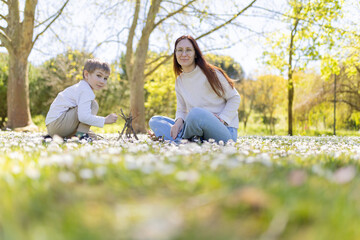 Mother and son building small teepee with branches in blooming meadow