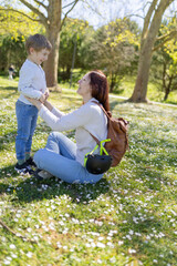 Fototapeta premium Mother kneeling on grass holding her son's hands in park