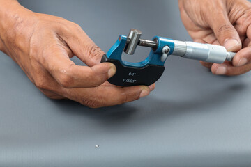 Hand holding analogue micrometer or diff micrometer quality control check roundness tube over grey table. use screw gauge calipers analogue. quality control concept.
