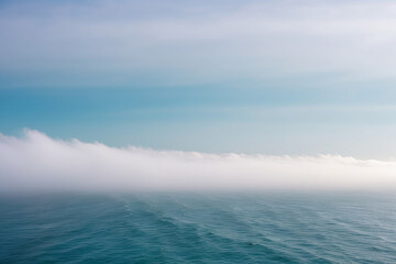 Obraz premium White Fog Bank Rolling Across a Teal Ocean Horizon