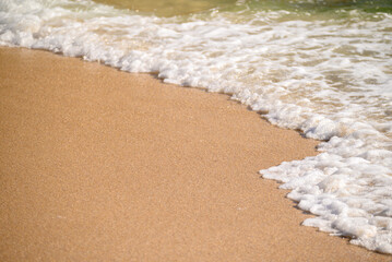 close up of golden sand and gentle sea foam on beach, summer concept background
