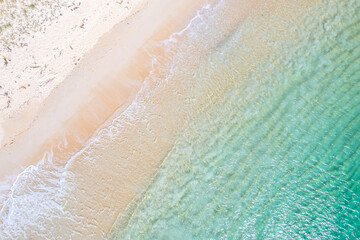 shore of a beach with pristine turquoise waters and golden sand. Zenithal aerial overhead view with drone, background for tropical summer concept.