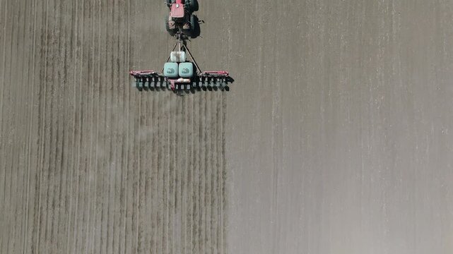 Drone footage of a farmer planting corn seeds in an iowa field in a red tractor