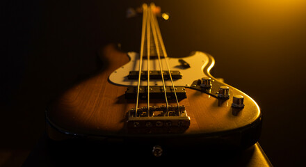 Bass guitar lies on a black background and golden light shines on it