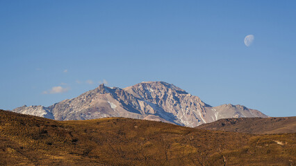 Snow-dusted Domuyo volcano peak under a clear blue sky with a visible moon. Neuquen, Argentina © Pajaros Volando