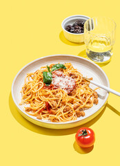 Spaghetti bolognese with tomato sauce, basil and parmesan cheese on yellow background