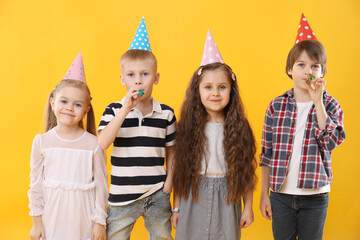 Children in conical paper hats with blowers on yellow background. Birthday surprise party
