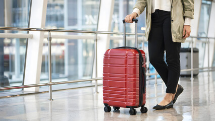 A female traveler of Caucasian descent stands in an airport terminal with her bright red suitcase, ideal for travel and luggage advertising