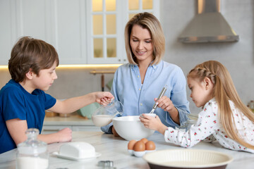 Mother and her kids making dough at white marble table in kitchen