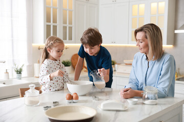 Mother and her kids making dough at white marble table in kitchen