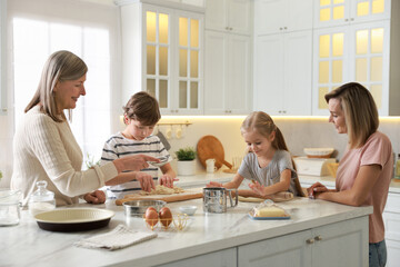 Little kids with their mother and grandmother making dough at white marble table in kitchen