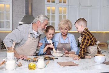 Grandparents and their grandkids cooking together at white marble table in kitchen