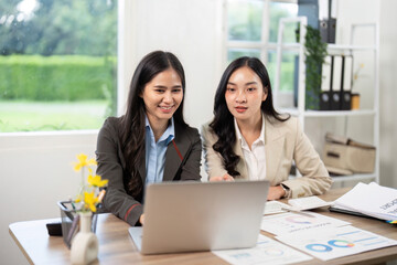 Team Collaboration and Data Analysis. Businesswomen engaging with laptop and reports.