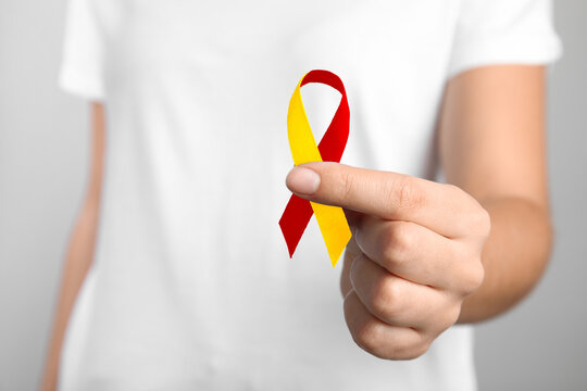 World Hepatitis Day. Woman with yellow-red awareness ribbon on light background, closeup - Powered by Adobe