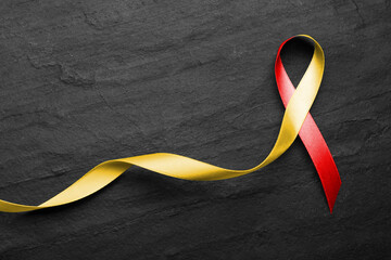 World Hepatitis Day. Yellow-red awareness ribbon on black table, top view