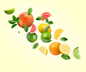 Different fresh citrus fruits and green leaves in air on beige background