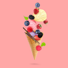 Yummy ice cream scoops, wafer cone and berries in air on pink background