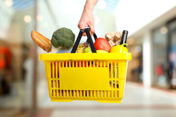 Man holding shopping basket with different food products at supermarket, closeup