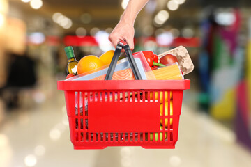 Man holding shopping basket with different food products at supermarket, closeup
