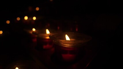 Glowing candle flames illuminate dark night peaceful remembrance hope memory faith light spiritual warmth comfort solace devotion prayer candles votive offering. 4k vidios - Powered by Adobe