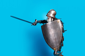Elderly man in medieval armor with sword and shield posing against blue background