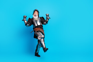 Elderly man in knight costume joyously posing on vibrant blue background