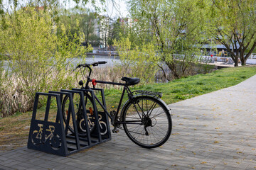 Bicycle parked in modern metal rack on riverside path surrounded by spring greenery.