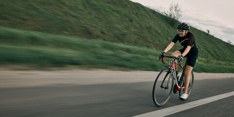 Fototapeta premium Sporty girl on racing bike moving fast along highway, blurred background and sharp bike frame emphasize action and determination. Concept of energy, training, sport, movement.