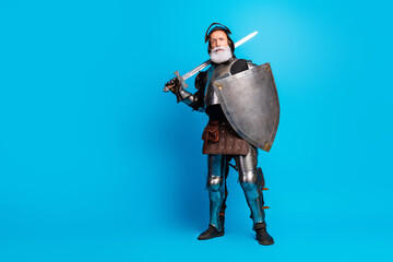 Elderly man dressed as a knight in medieval armor with sword and shield, standing confidently...