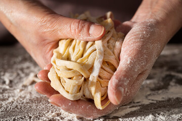 Caucasian female hands holding raw fettuccine noodles after drying