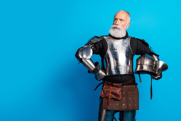 Naklejka premium Elderly bearded man wearing medieval-style metal armor posing against a blue background, representing historical themes and noble traits