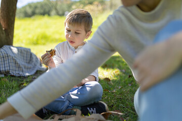 Obraz premium Child eating sandwich at a picnic with family in a park
