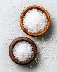 Two wooden bowls filled with coarse sea salt from above on a light grey surface food photography ingredient cooking seasoning