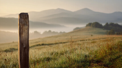 Rustic Wooden Stake Standing in Tall Grass with Wildflowers Against Rolling Hills and Misty Mountains at Dawn