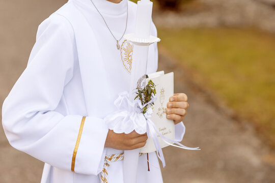 Young child in white communion robe holding a decorated candle during First Holy Communion. Polish Catholic tradition celebrating faith, purity, and spiritual growth.