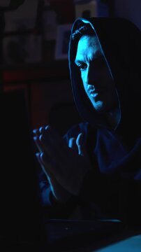 Anonymous hacker browsing the dark web on laptop in dimly lit room symbolizing illegal activity and cybercrime