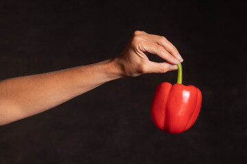 female hand holding a juicy large red pepper by the green stem