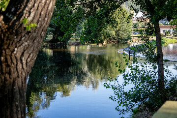 A serene river scene featuring a small stone dam with water gently cascading over the edge, surrounded by greenery and reflected sunlight, creating a peaceful and natural atmosphere. Serta, Portugal.