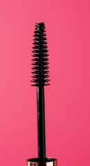Black mascara wand with bristles on vibrant pink background, close-up beauty product detail
