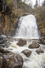 Korbu waterfall near Teletskoye lake in Altai Russia. Powerful stream of water falling from cliff surrounded by wild forest