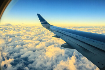 Obraz premium View from airplane window showing wing over clouds against a gradient blue and yellow sky